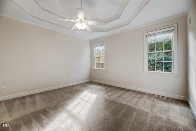 carpeted empty room featuring a raised ceiling, ornamental molding, a wealth of natural light, and ceiling fan