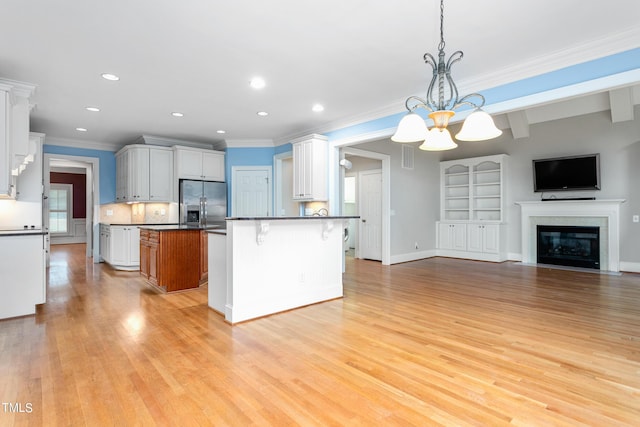 kitchen featuring stainless steel fridge, hanging light fixtures, white cabinetry, a kitchen bar, and a kitchen island