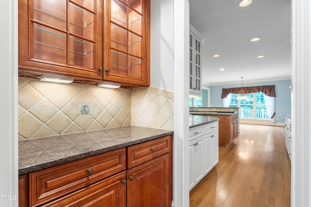 kitchen featuring decorative light fixtures, backsplash, light hardwood / wood-style flooring, and dark stone counters