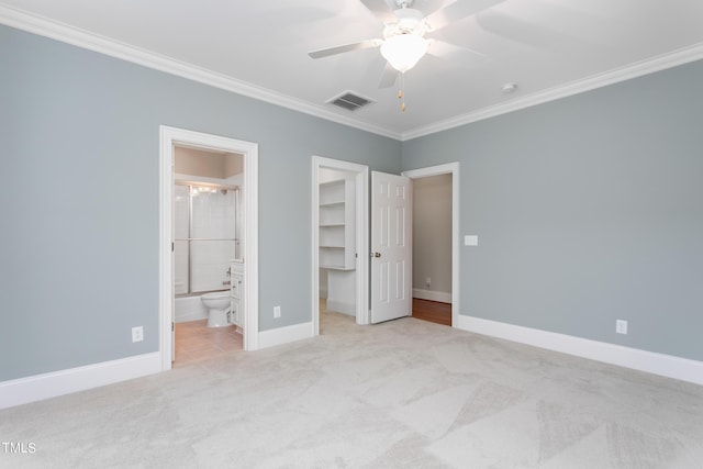 unfurnished bedroom featuring crown molding, a walk in closet, light colored carpet, ceiling fan, and connected bathroom