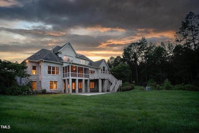 back house at dusk with a deck, a balcony, a patio, and a lawn