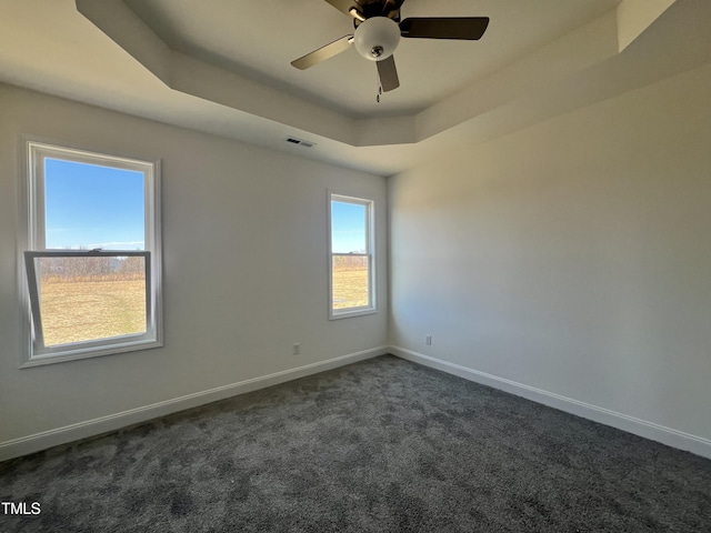 empty room with dark colored carpet, ceiling fan, and a tray ceiling