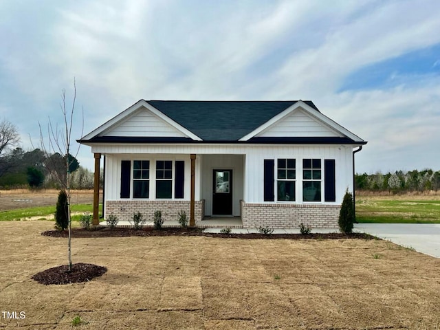 view of front of property featuring brick siding, covered porch, and roof with shingles