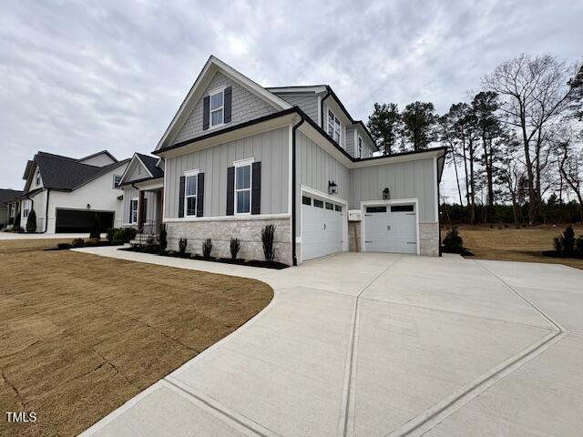 view of front facade featuring driveway, stone siding, an attached garage, and board and batten siding