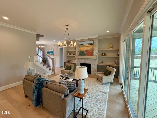 living area with a large fireplace, stairs, a chandelier, and light wood-style floors