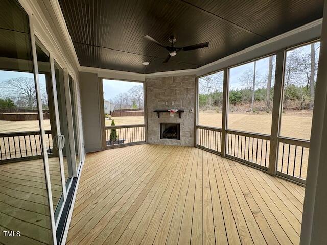 unfurnished sunroom with ceiling fan, an outdoor stone fireplace, and wood ceiling