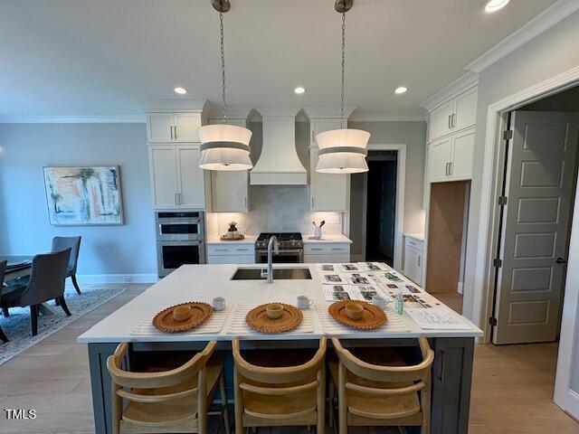 kitchen featuring custom exhaust hood, tasteful backsplash, appliances with stainless steel finishes, ornamental molding, and a sink