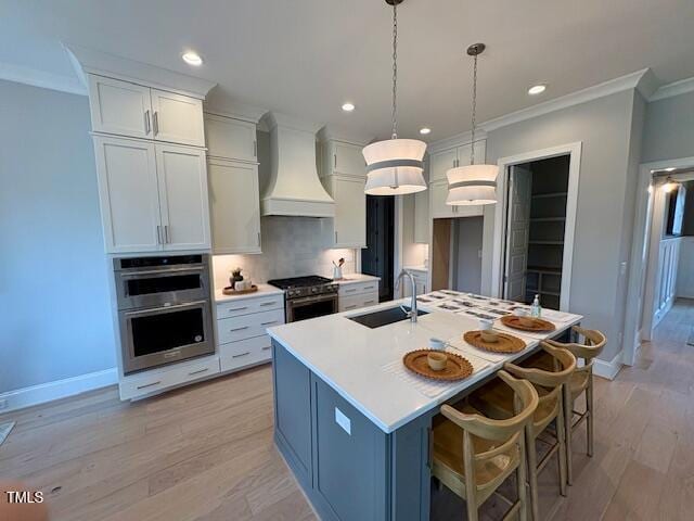 kitchen featuring a kitchen island with sink, stainless steel appliances, a sink, ornamental molding, and custom exhaust hood