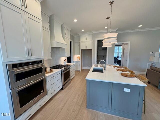 kitchen featuring a sink, light countertops, appliances with stainless steel finishes, light wood finished floors, and custom range hood