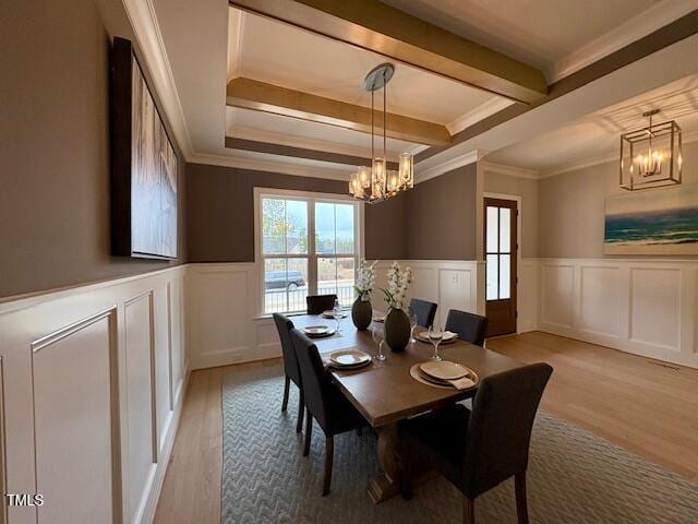 dining room with beam ceiling, crown molding, light wood-style flooring, wainscoting, and a chandelier