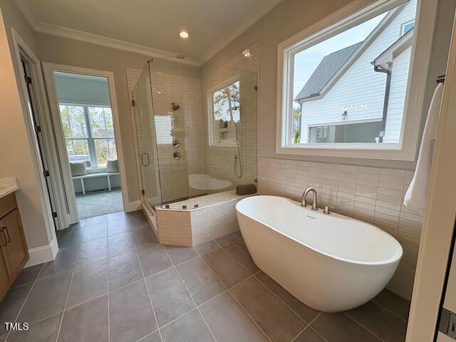 full bath featuring tile patterned flooring, vanity, a freestanding bath, a stall shower, and crown molding