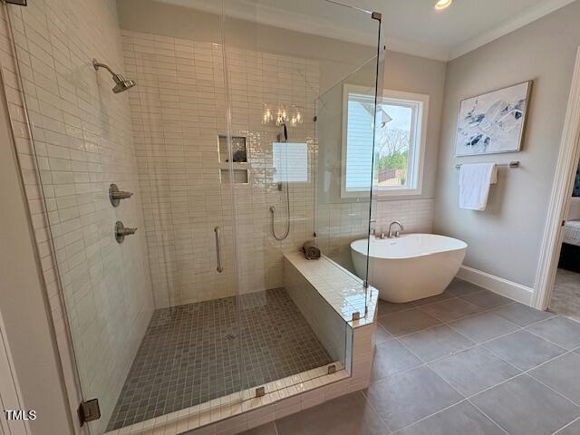 bathroom with crown molding, a freestanding bath, a stall shower, tile patterned flooring, and baseboards