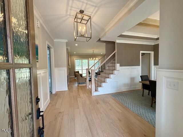 entryway featuring a wainscoted wall, stairway, wood finished floors, and an inviting chandelier