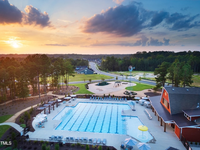 pool at dusk featuring a water slide and a patio area