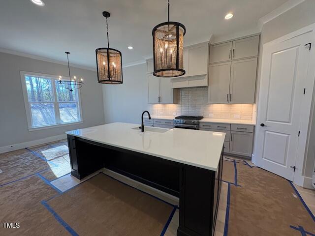 kitchen featuring sink, decorative light fixtures, stainless steel range, a kitchen island with sink, and backsplash