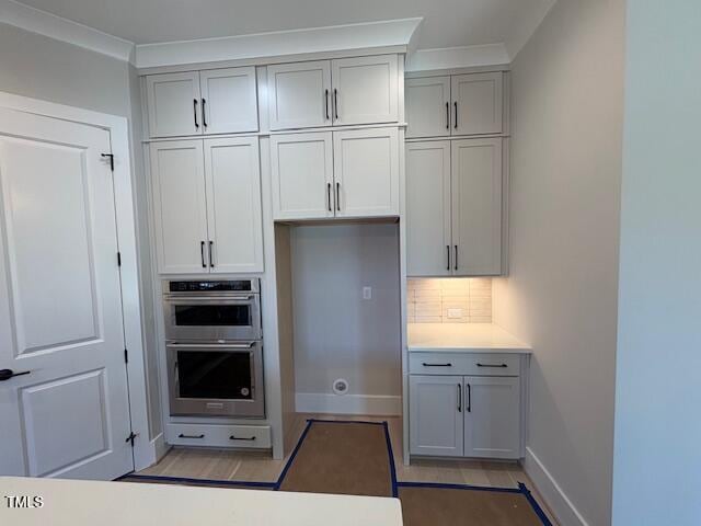 kitchen featuring gray cabinetry, decorative backsplash, crown molding, and stainless steel double oven