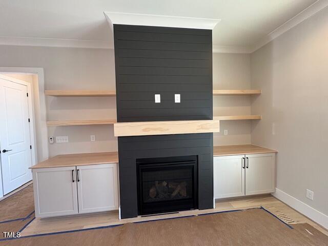 unfurnished living room featuring crown molding, a large fireplace, and light hardwood / wood-style floors