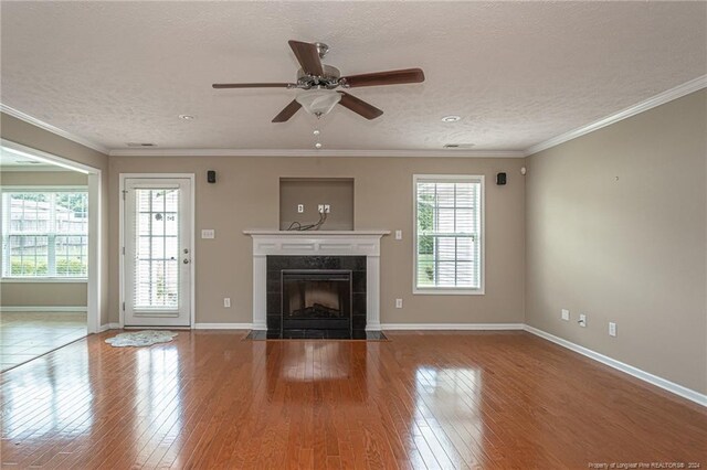 unfurnished living room featuring ceiling fan, hardwood / wood-style floors, ornamental molding, a tile fireplace, and a textured ceiling