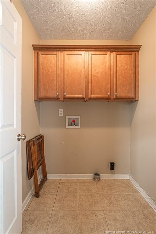 clothes washing area with hookup for a washing machine, cabinets, light tile patterned floors, and a textured ceiling