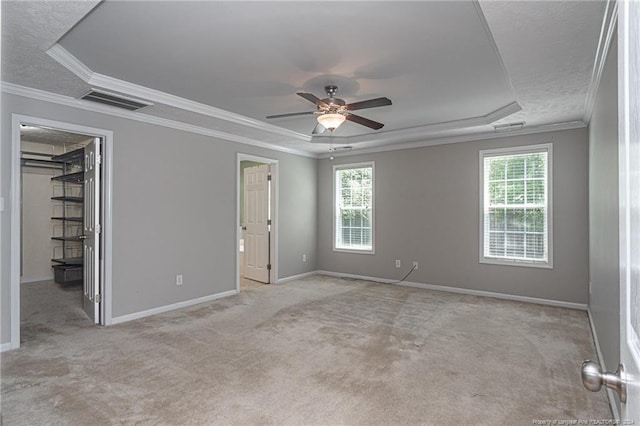 unfurnished bedroom with visible vents, carpet floors, a tray ceiling, ornamental molding, and a walk in closet