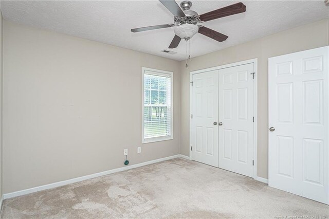 unfurnished bedroom with light carpet, a textured ceiling, a closet, and ceiling fan