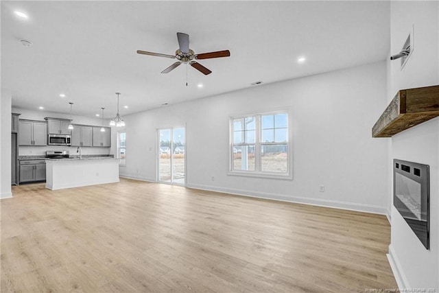 unfurnished living room with sink, ceiling fan with notable chandelier, and light wood-type flooring