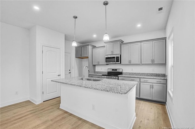 kitchen featuring sink, light stone counters, an island with sink, pendant lighting, and stainless steel appliances