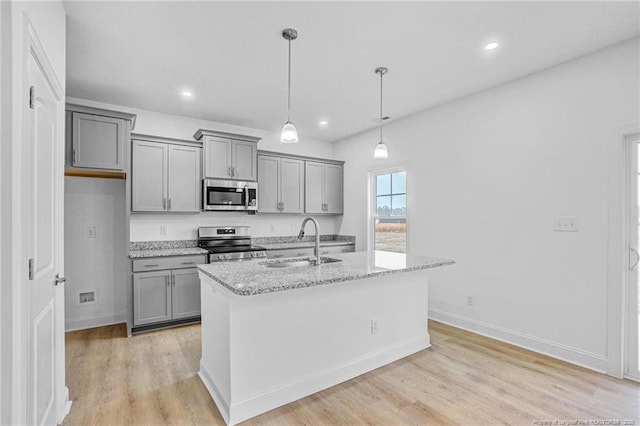 kitchen featuring sink, hanging light fixtures, a kitchen island with sink, stainless steel appliances, and light stone countertops