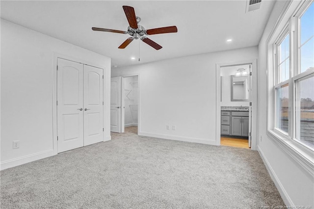 unfurnished bedroom with connected bathroom, light colored carpet, a closet, and ceiling fan