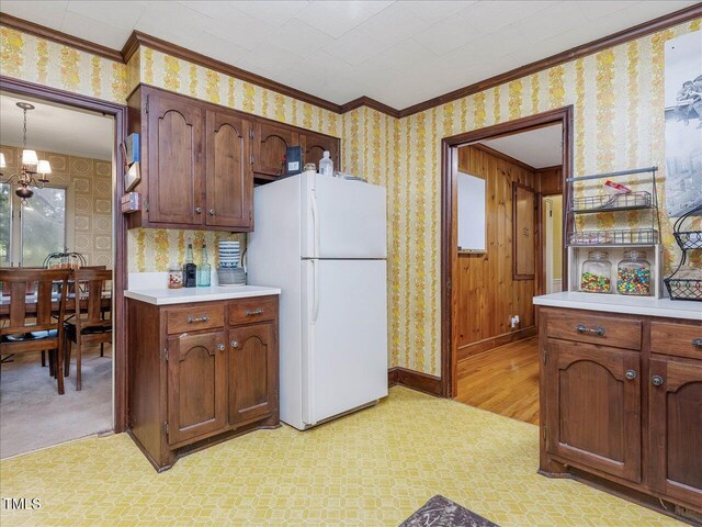 kitchen with white fridge, crown molding, an inviting chandelier, light carpet, and decorative light fixtures