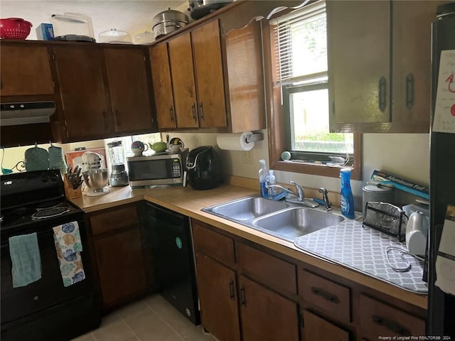 kitchen with light tile patterned floors, light countertops, a sink, under cabinet range hood, and black appliances