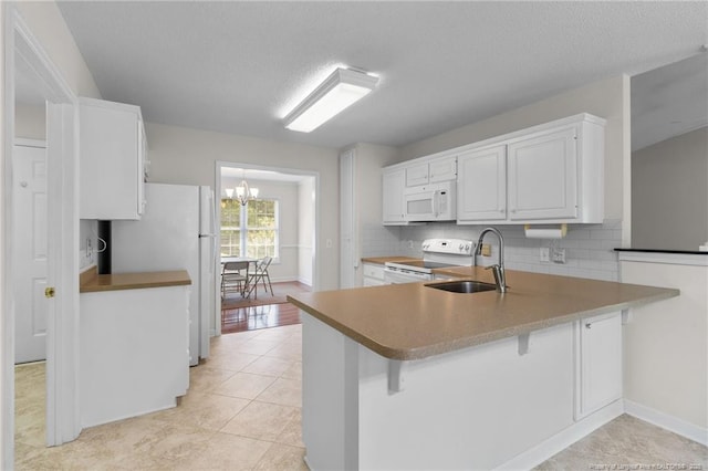 kitchen with a chandelier, white appliances, a peninsula, decorative backsplash, and a sink