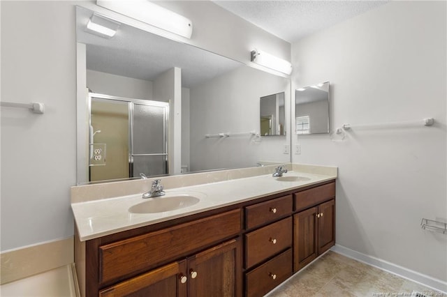 bathroom with double vanity, baseboards, a sink, and a stall shower