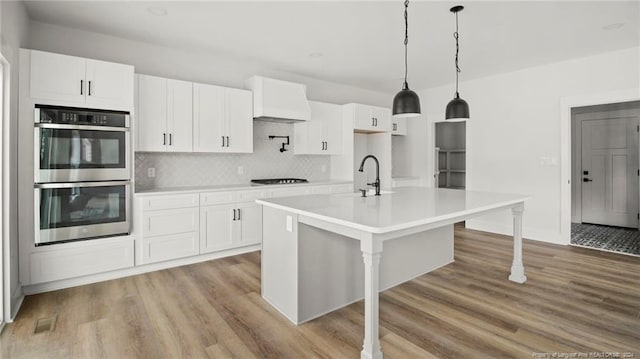 kitchen with white cabinets, light hardwood / wood-style floors, double oven, and an island with sink