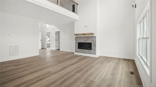 unfurnished living room featuring a towering ceiling, light hardwood / wood-style floors, and plenty of natural light