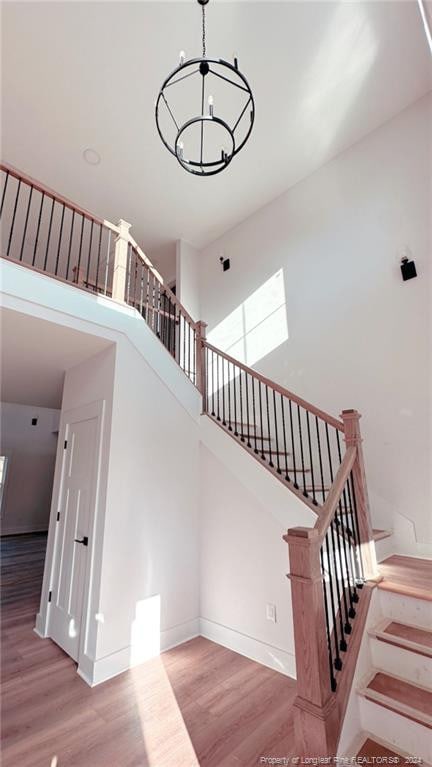 stairs with a towering ceiling, wood-type flooring, and a notable chandelier