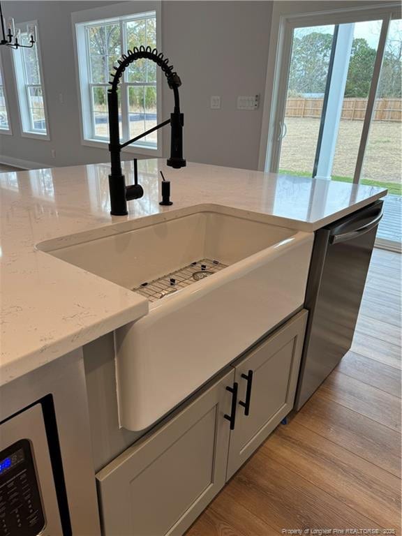 kitchen with light stone counters, light wood-style floors, dishwasher, and a sink