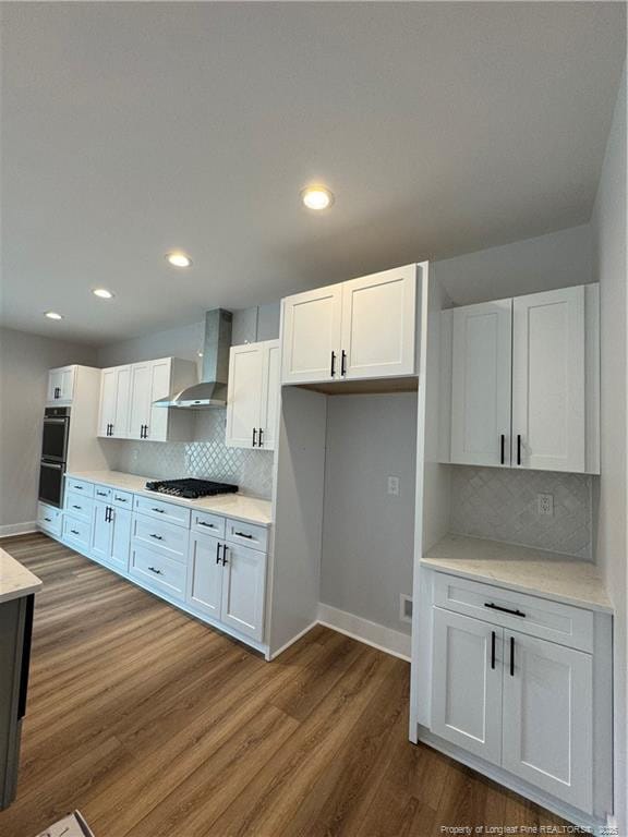 kitchen featuring appliances with stainless steel finishes, dark wood-type flooring, light countertops, wall chimney range hood, and white cabinetry