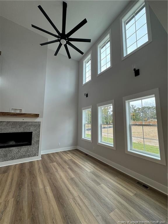 unfurnished living room featuring a fireplace, a towering ceiling, visible vents, baseboards, and light wood-type flooring