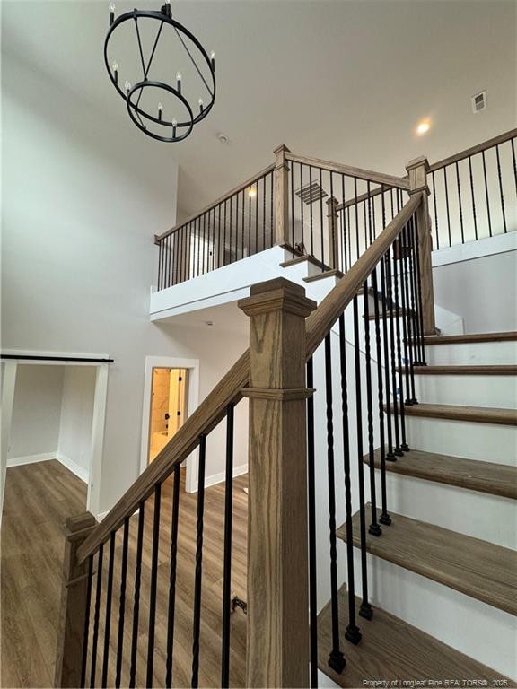 staircase with a notable chandelier, visible vents, a towering ceiling, wood finished floors, and baseboards