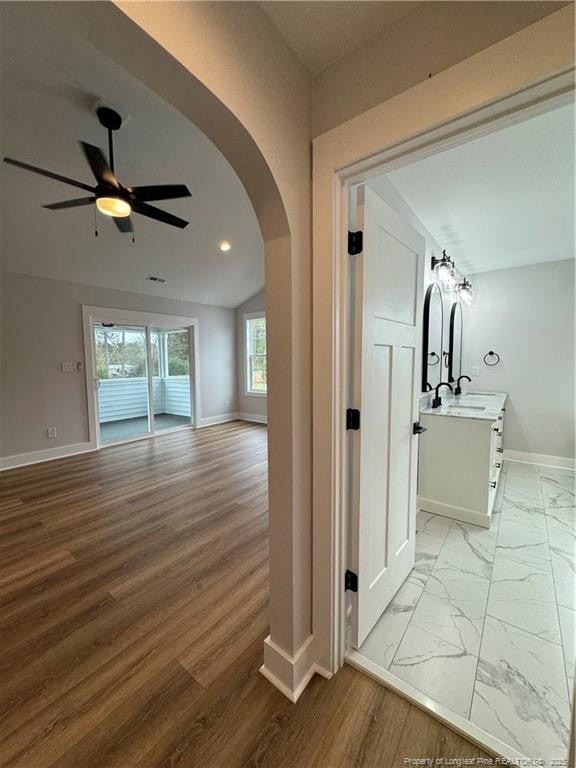 corridor featuring arched walkways, marble finish floor, a sink, and baseboards