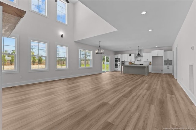 unfurnished living room featuring baseboards, a notable chandelier, recessed lighting, and light wood-type flooring