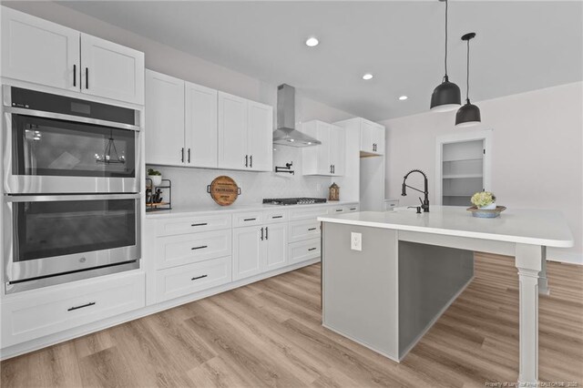 kitchen with gas stovetop, double oven, a sink, light wood-style floors, and wall chimney exhaust hood