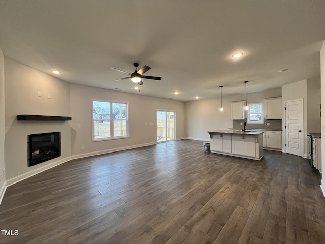 unfurnished living room with sink, plenty of natural light, dark hardwood / wood-style floors, and ceiling fan