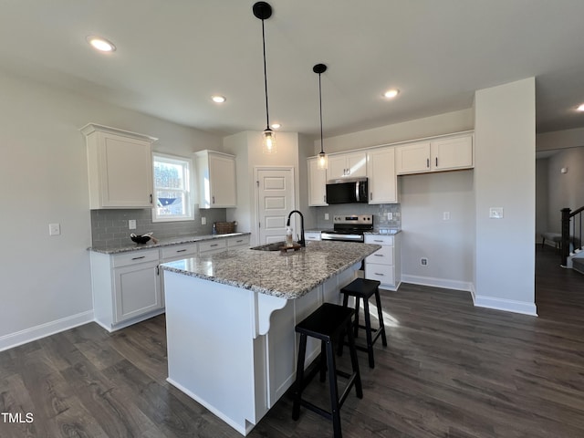 kitchen with a kitchen island with sink, light stone countertops, stainless steel appliances, and white cabinets