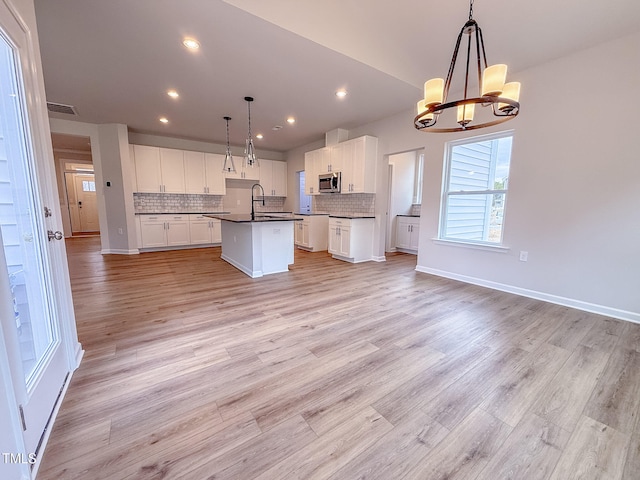 kitchen featuring decorative backsplash, a center island with sink, white cabinets, and decorative light fixtures