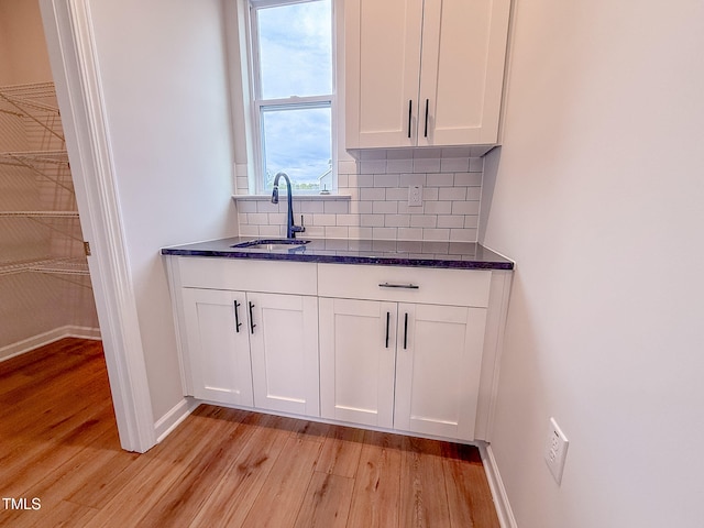 bar featuring sink, dark stone countertops, backsplash, white cabinets, and light wood-type flooring