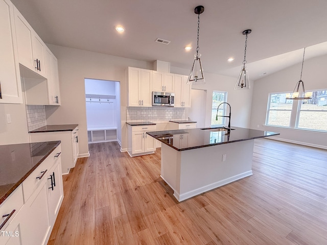 kitchen featuring sink, white cabinets, hanging light fixtures, light hardwood / wood-style floors, and a center island with sink