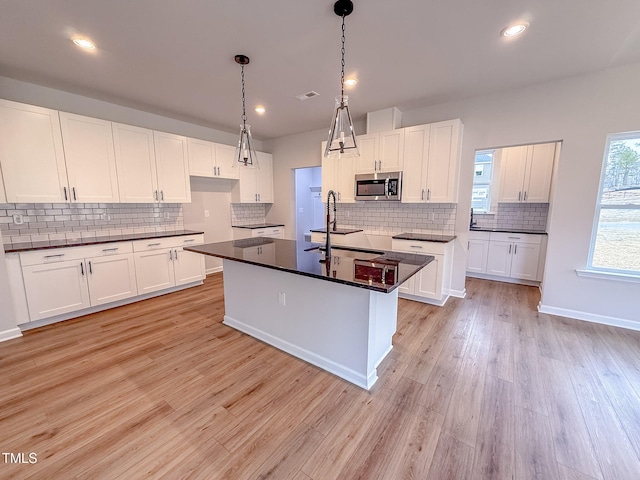 kitchen featuring hanging light fixtures, white cabinetry, and a center island with sink