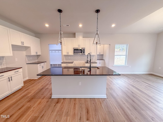 kitchen with decorative light fixtures, sink, a center island with sink, and white cabinets